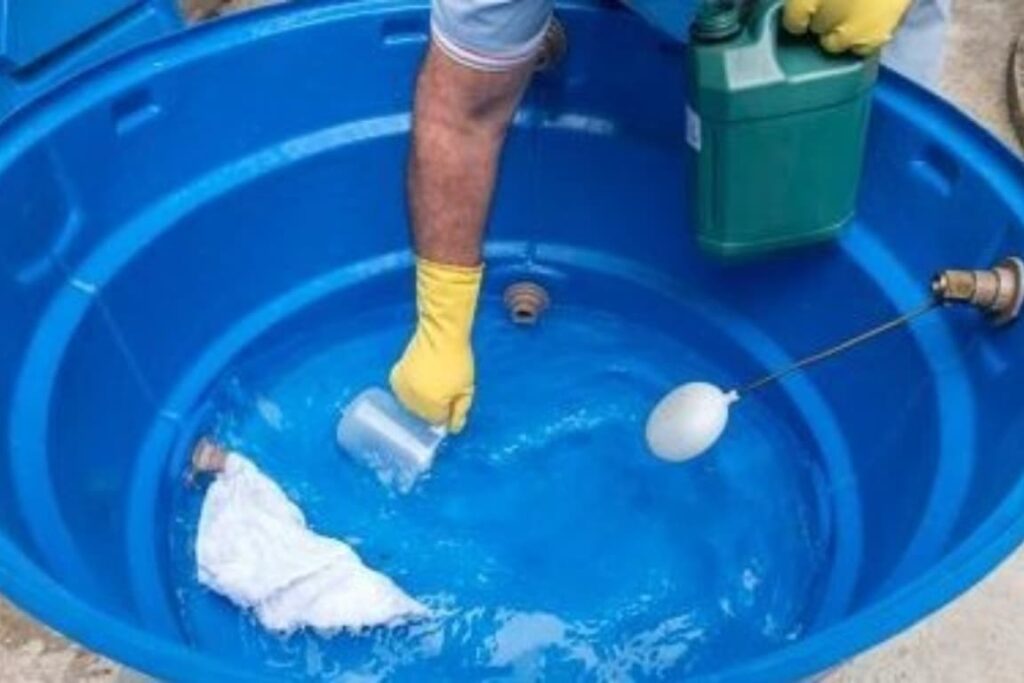 Imagem de um homem usando luvas amarelas, limpando uma caixa d'água redonda e azul. A cena destaca a importância de manter a caixa d'água limpa para garantir a qualidade da água consumida e prevenir a proliferação de algas e bactérias.